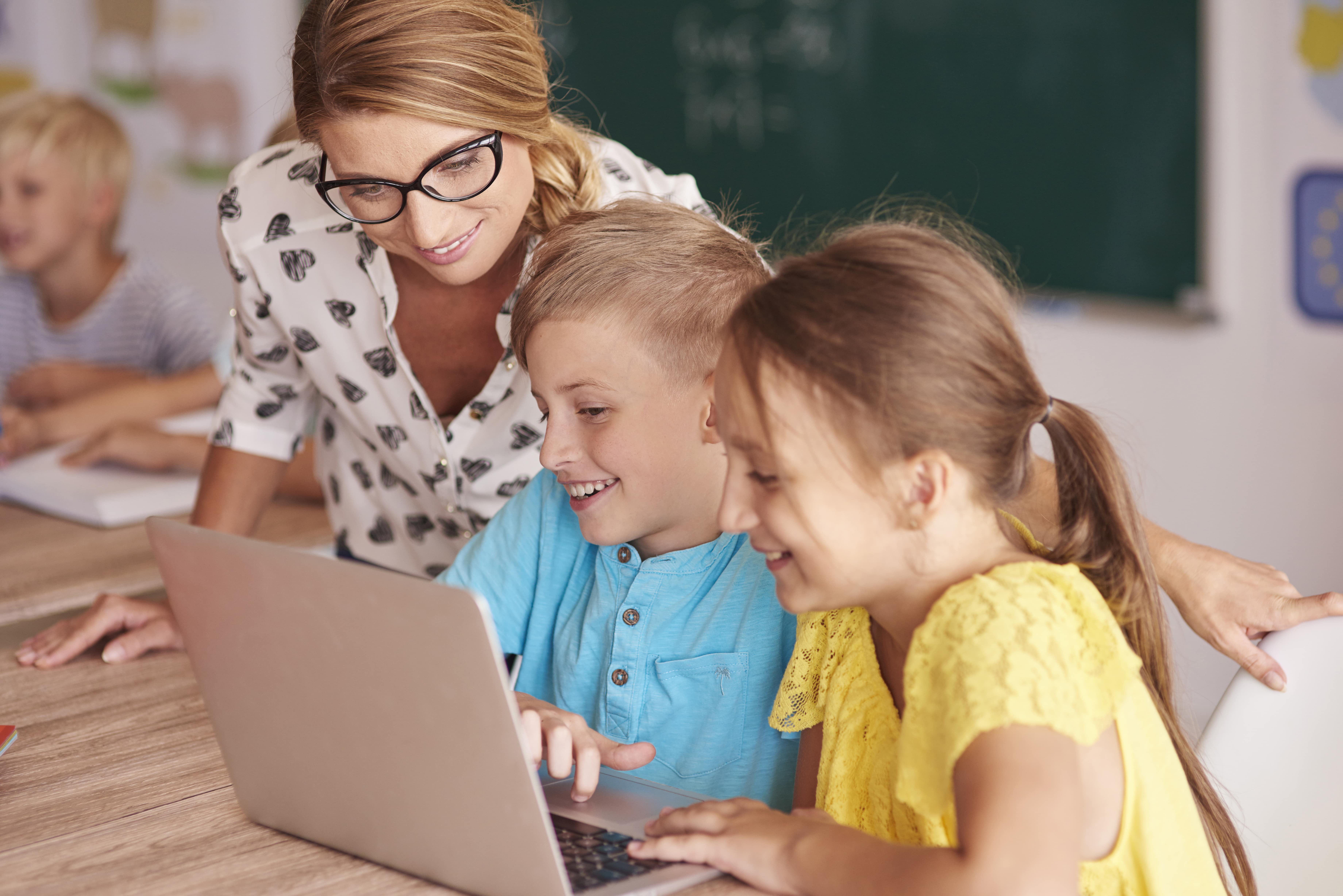 teacher with student using laptop in classroom