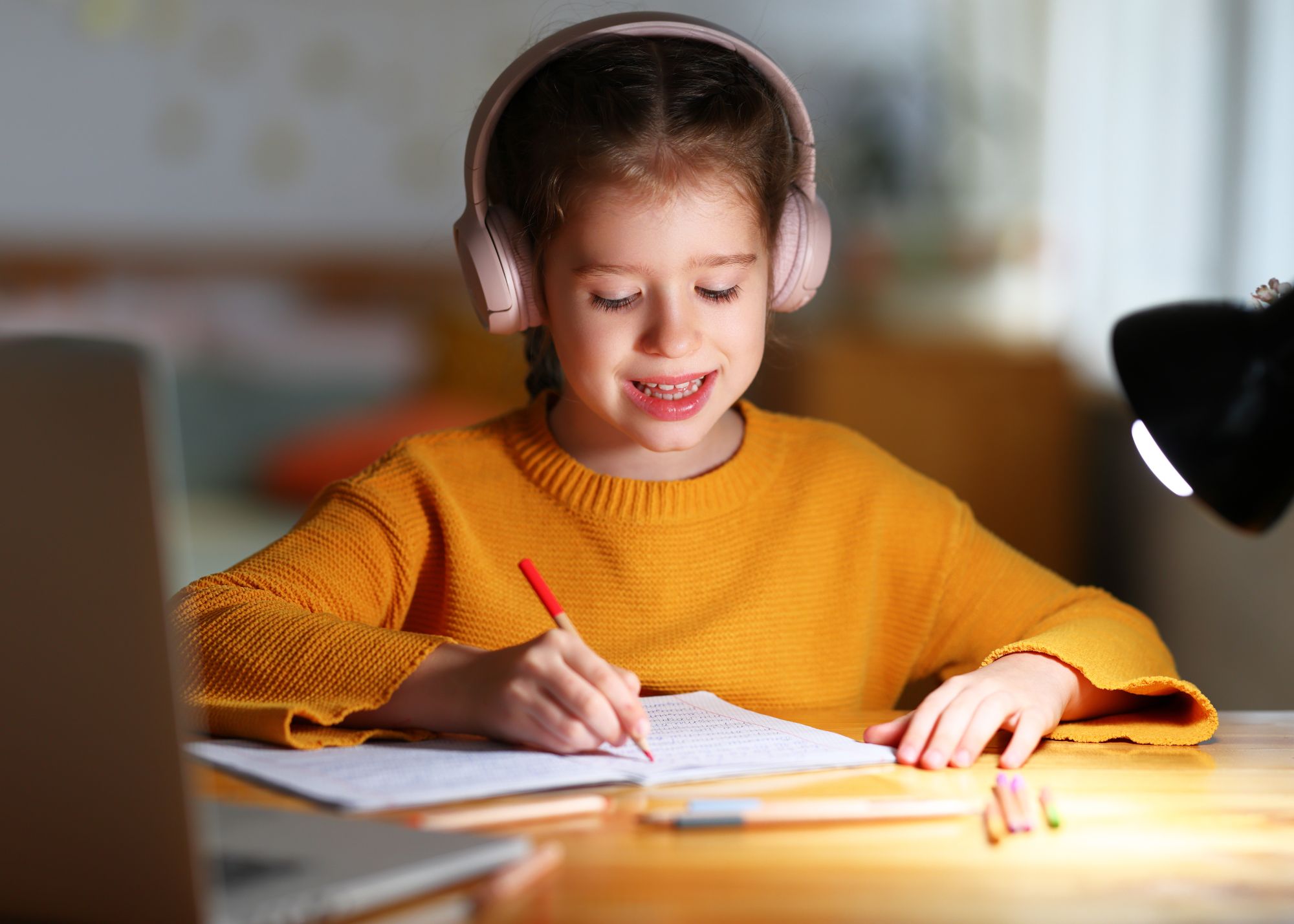 little girl doing homework while listening to lessons on headphones